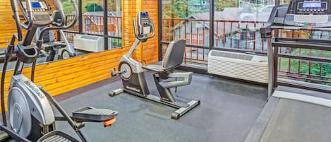 A gym with cardio machines, a treadmill, and large windows offering a view of the outdoors.