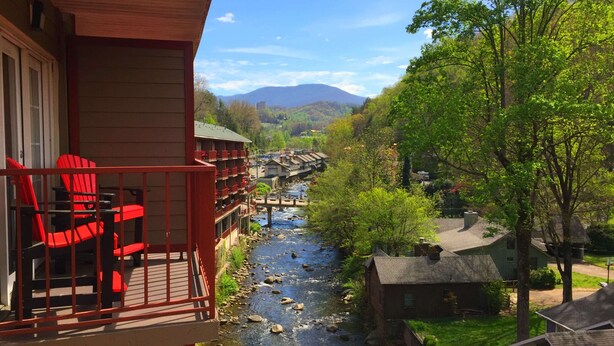 A riverside view from a balcony with red chairs, a wooden deck, and a bridge in the background. - Baymont by Wyndham Gatlinburg On The River (Gatlinburg)
