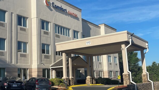 A Comfort Suites hotel with a covered entrance, parking area, and a clear blue sky.