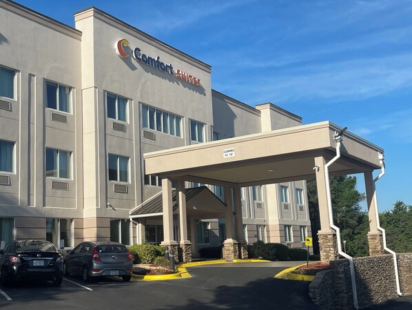 Un hotel Comfort Suites con entrada cubierta, zona de estacionamiento y un cielo azul despejado.