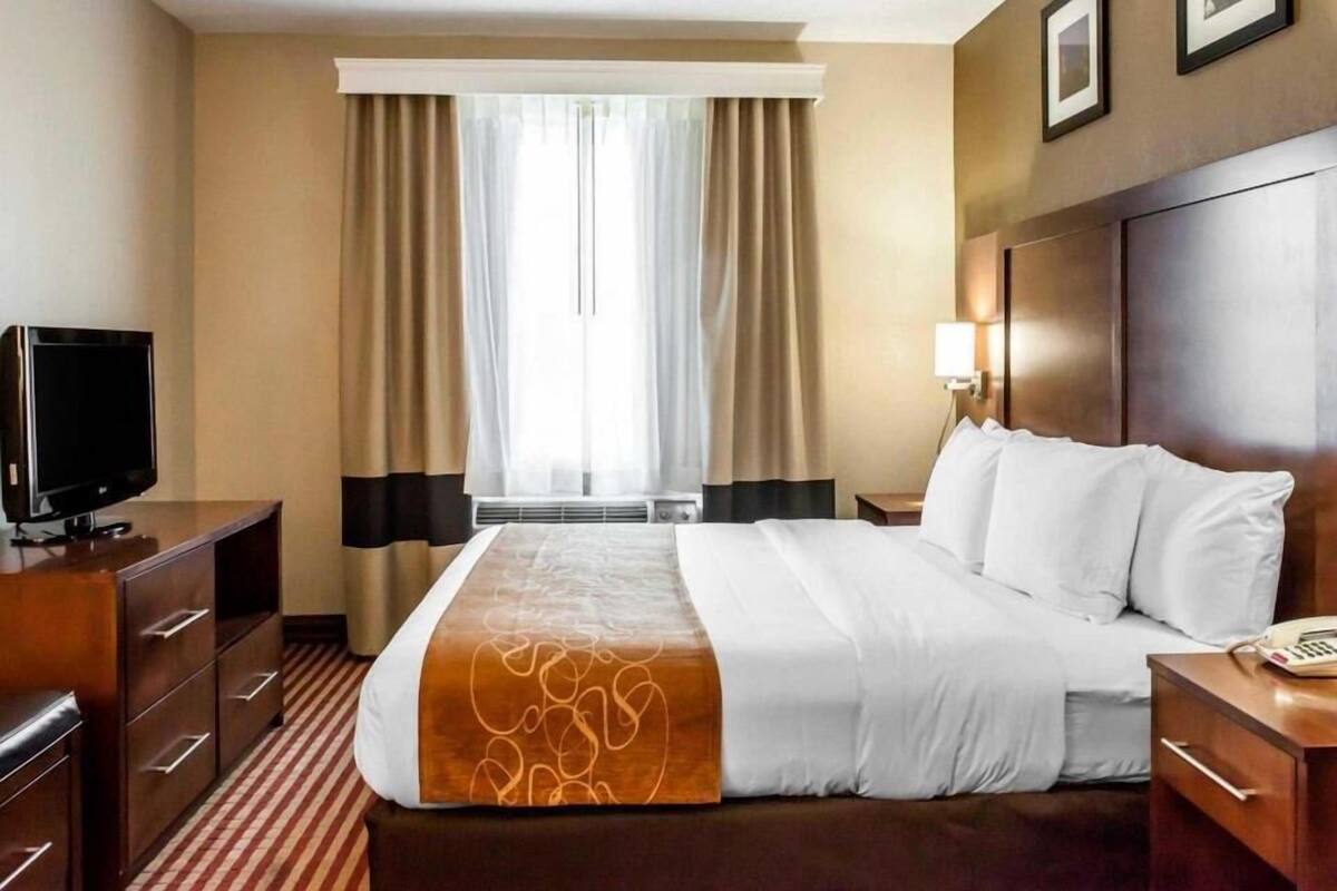 A hotel room with a bed, a television, a desk, and a window with curtains.