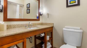A bathroom with a wooden vanity, sink, and toilet. There is a mirror above the sink, and a framed picture on the wall.