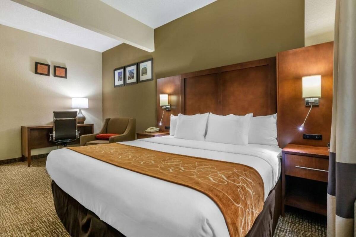 A hotel room with a large bed, a desk with a computer, a chair, and two bedside lamps.