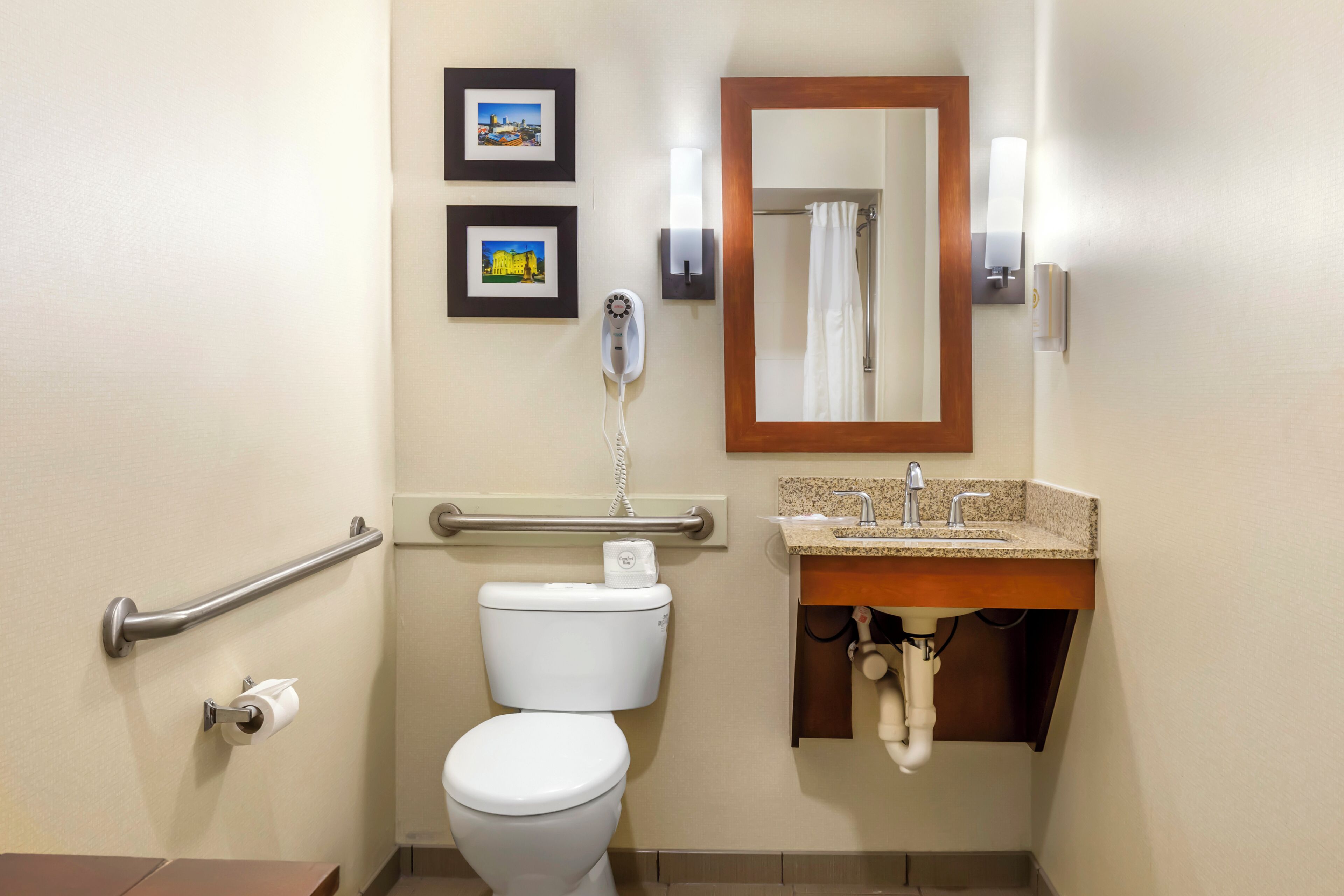 A bathroom with a toilet, a hand dryer, a sink, a mirror, and two framed pictures on the wall.