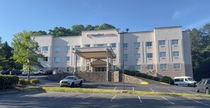 Un hotel llamado 'Comfort Suites' con entrada techada, estacionamiento y un muro de piedra.