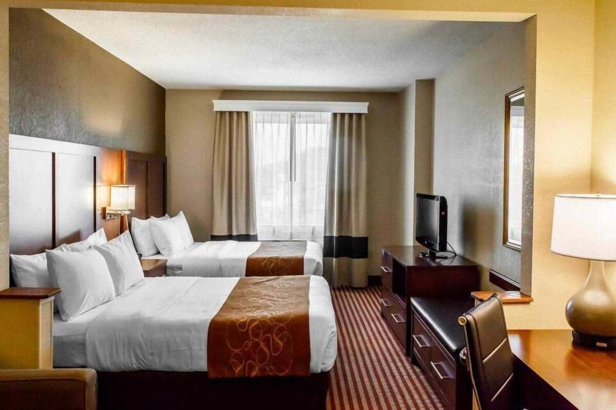 A hotel room with two beds, a TV, a desk, and a lamp.