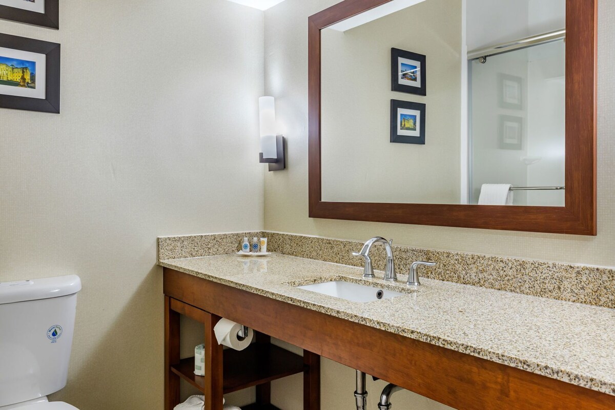 A bathroom with a toilet, sink, mirror, and framed pictures on the wall.