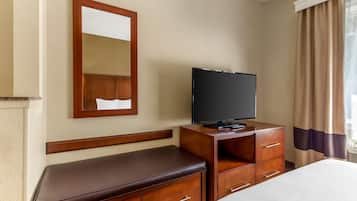 A hotel room with a bed, a wooden dresser, a television, a bench, and a mirror.