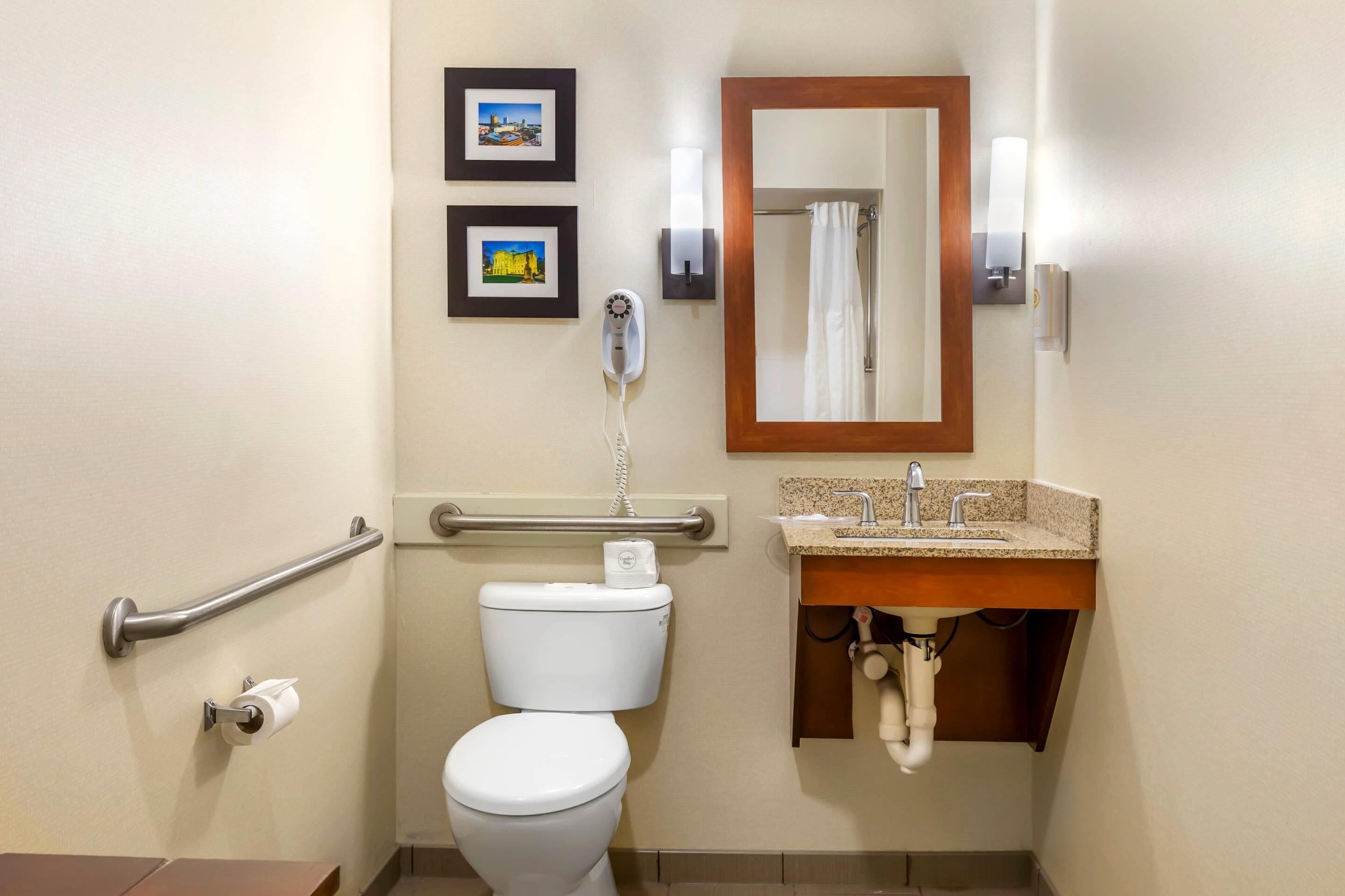 A bathroom with a toilet, a hand dryer, a sink, and a mirror.