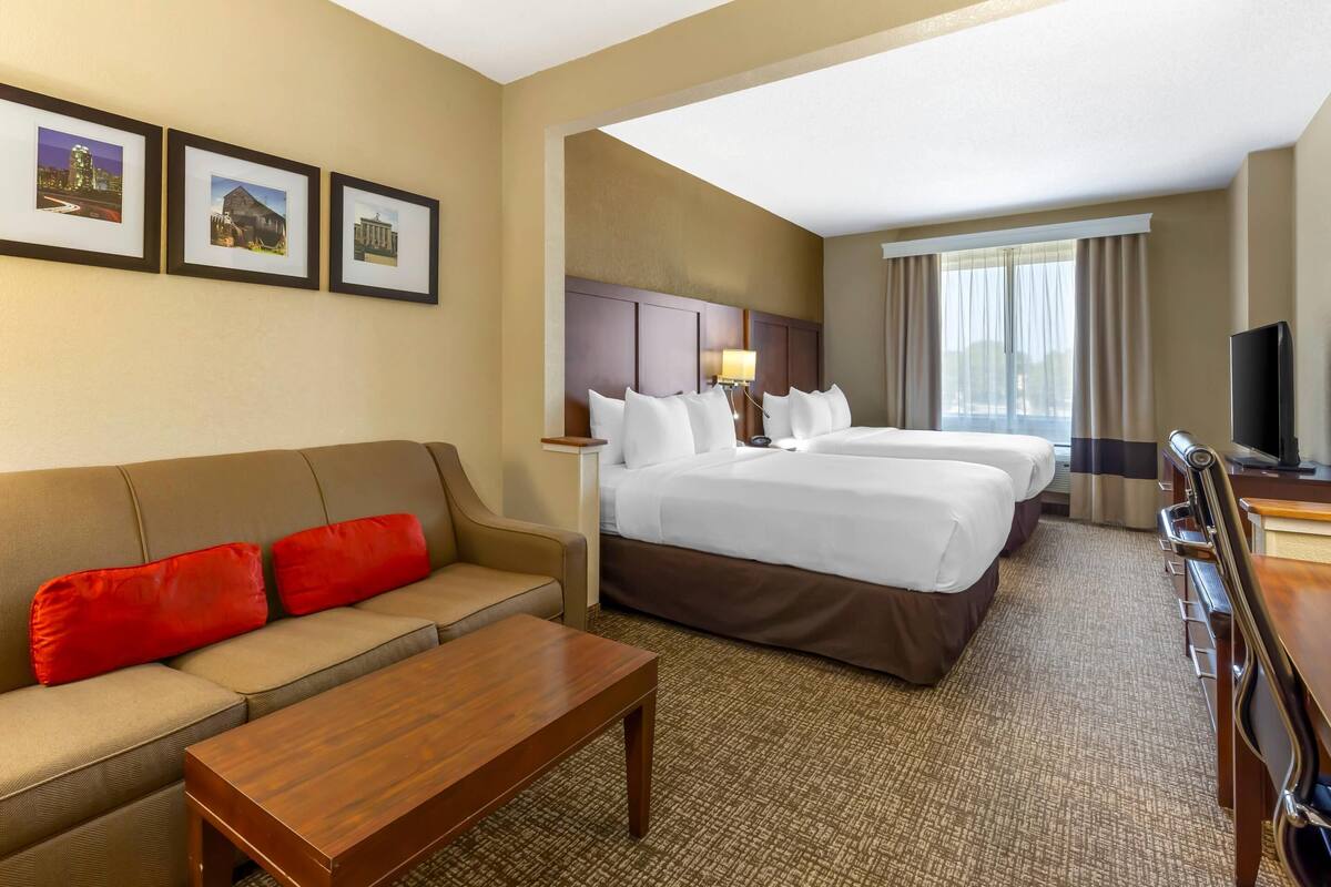 A hotel room with a sofa, two beds, a desk, and a TV.