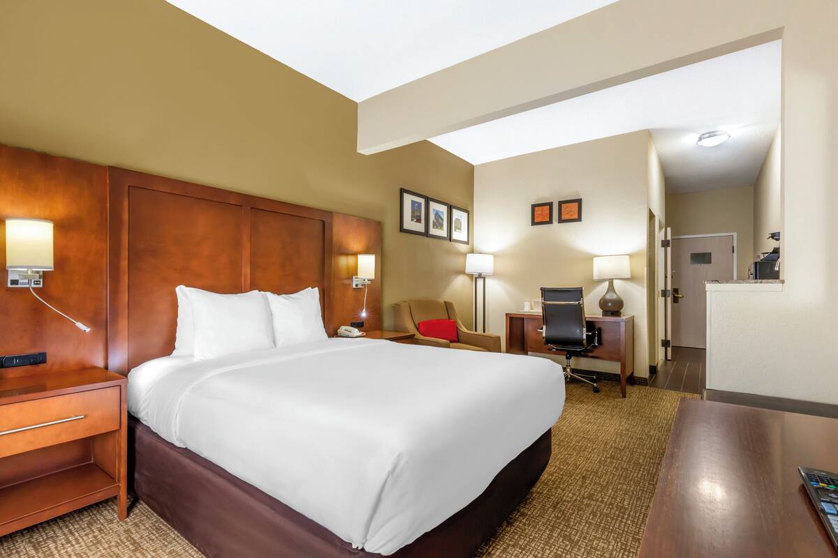 A hotel room with a large bed, bedside tables, a desk, a chair, a TV, and a lamp.