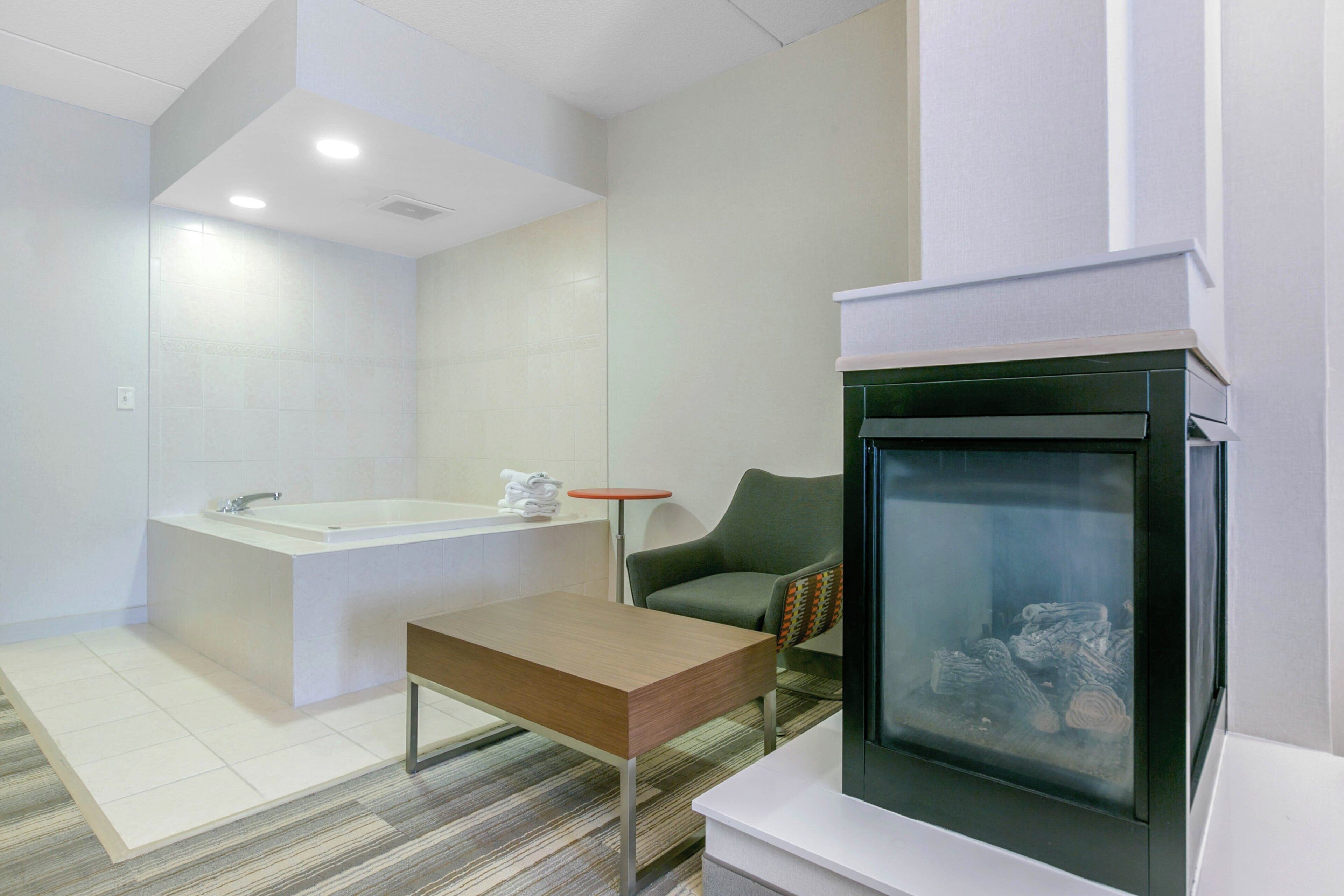 A modern bathroom with a bathtub, a toilet, and a sink. There is a small table and a chair in the room.