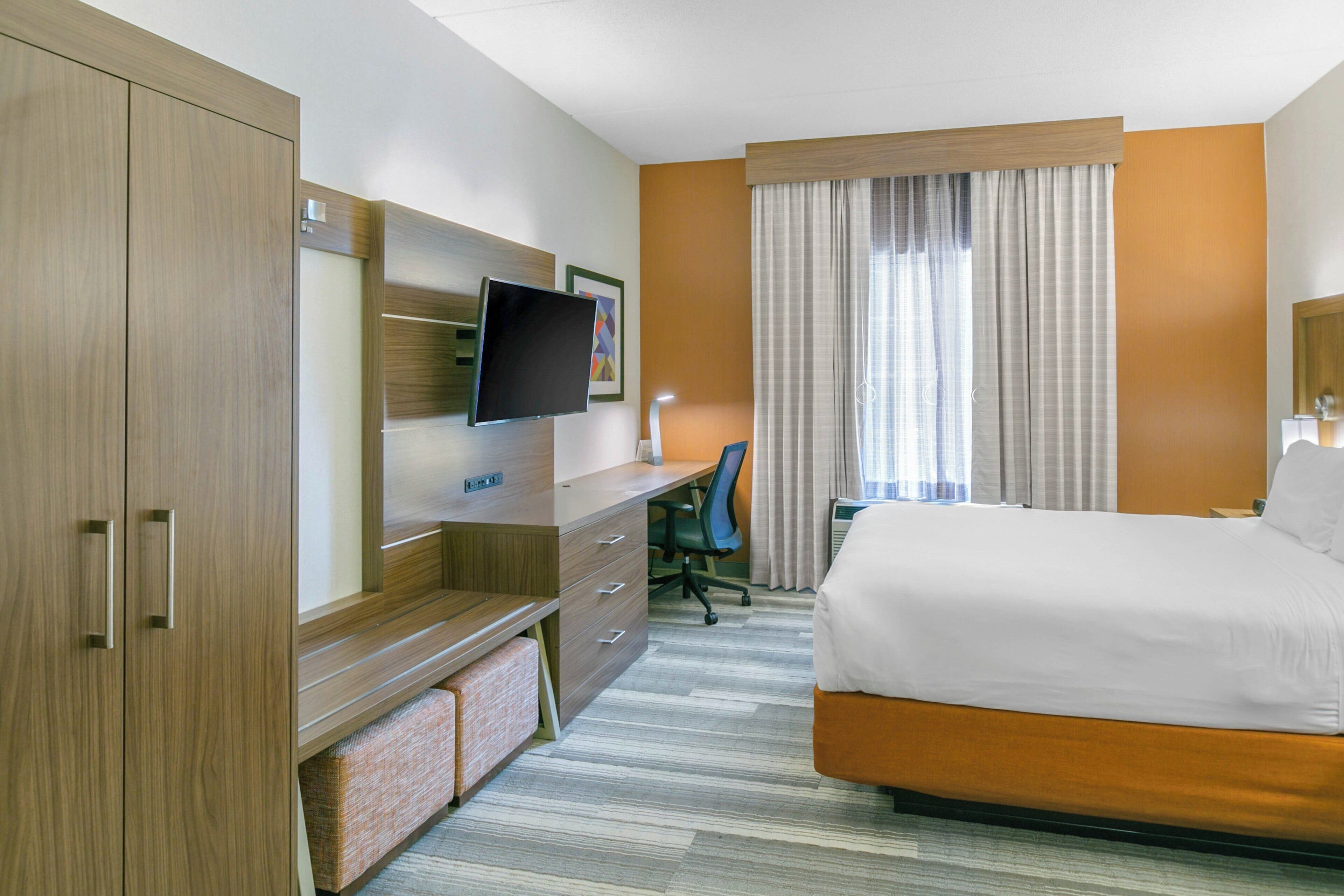 Una habitación de hotel con cama, escritorio con silla, televisor y armario.