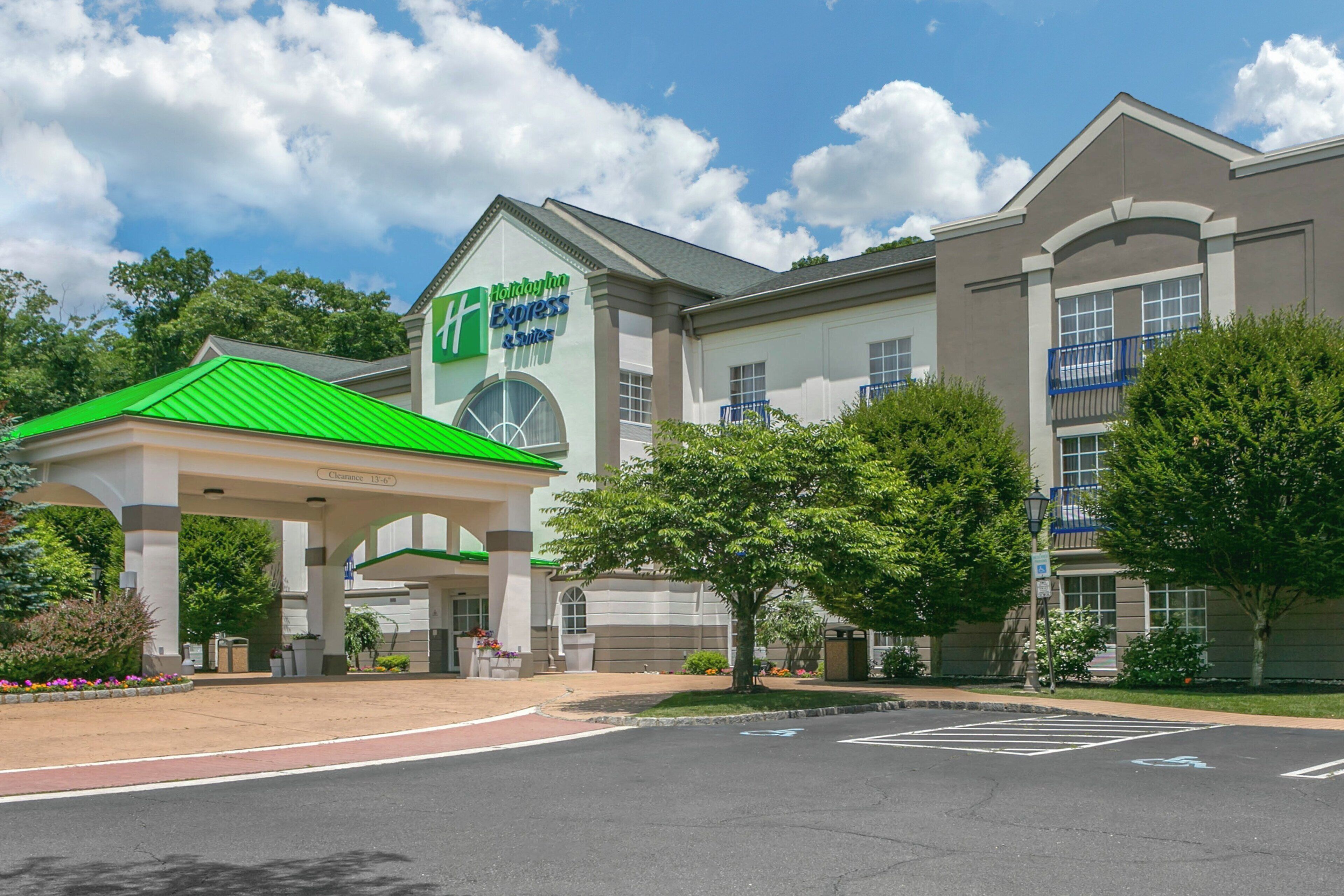 A Holiday Inn Express & Suites with a green-roofed entrance pavilion, parking lot, and surrounding greenery.