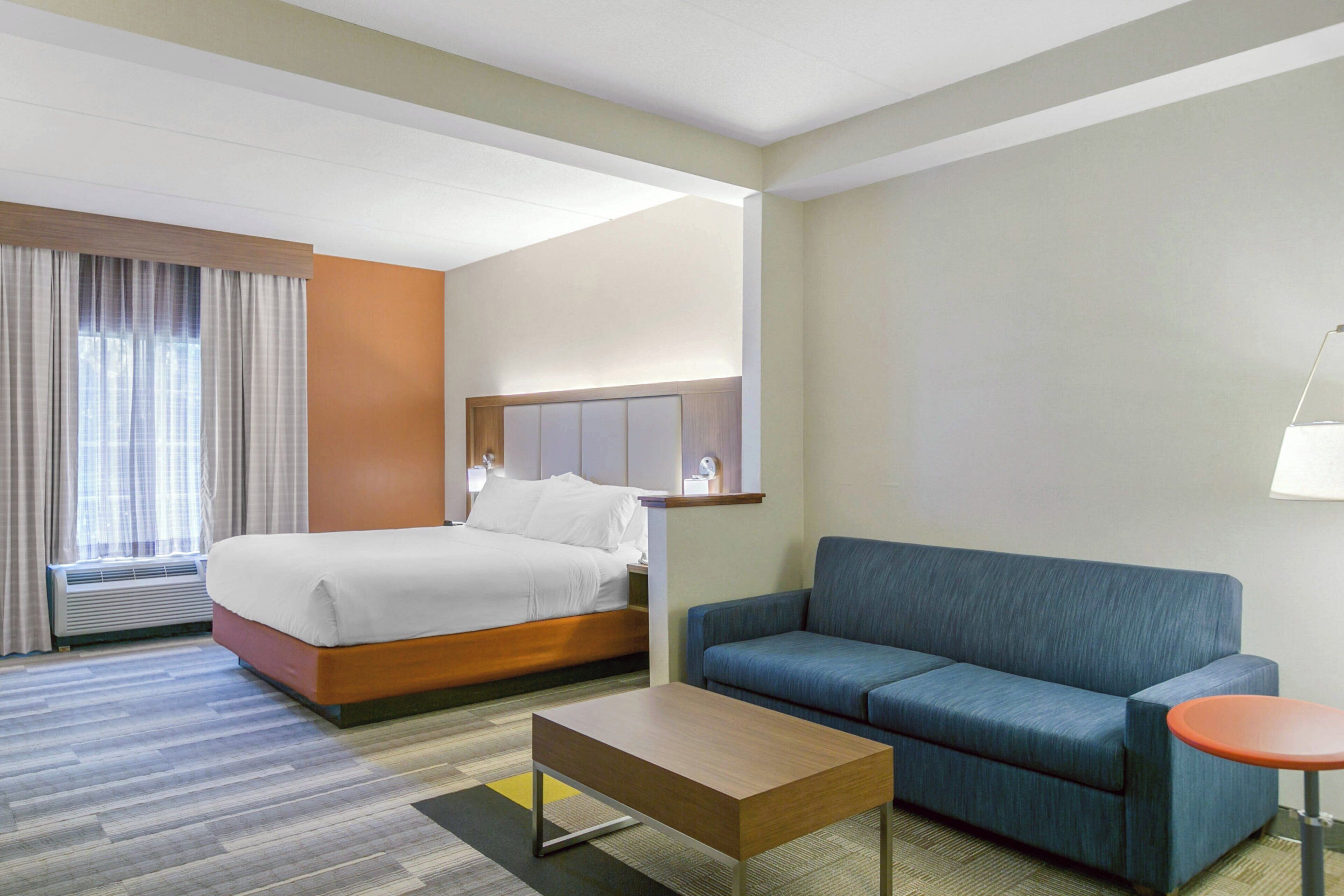 A hotel room with a bed, a sofa, a coffee table, a lamp, and a window with curtains.