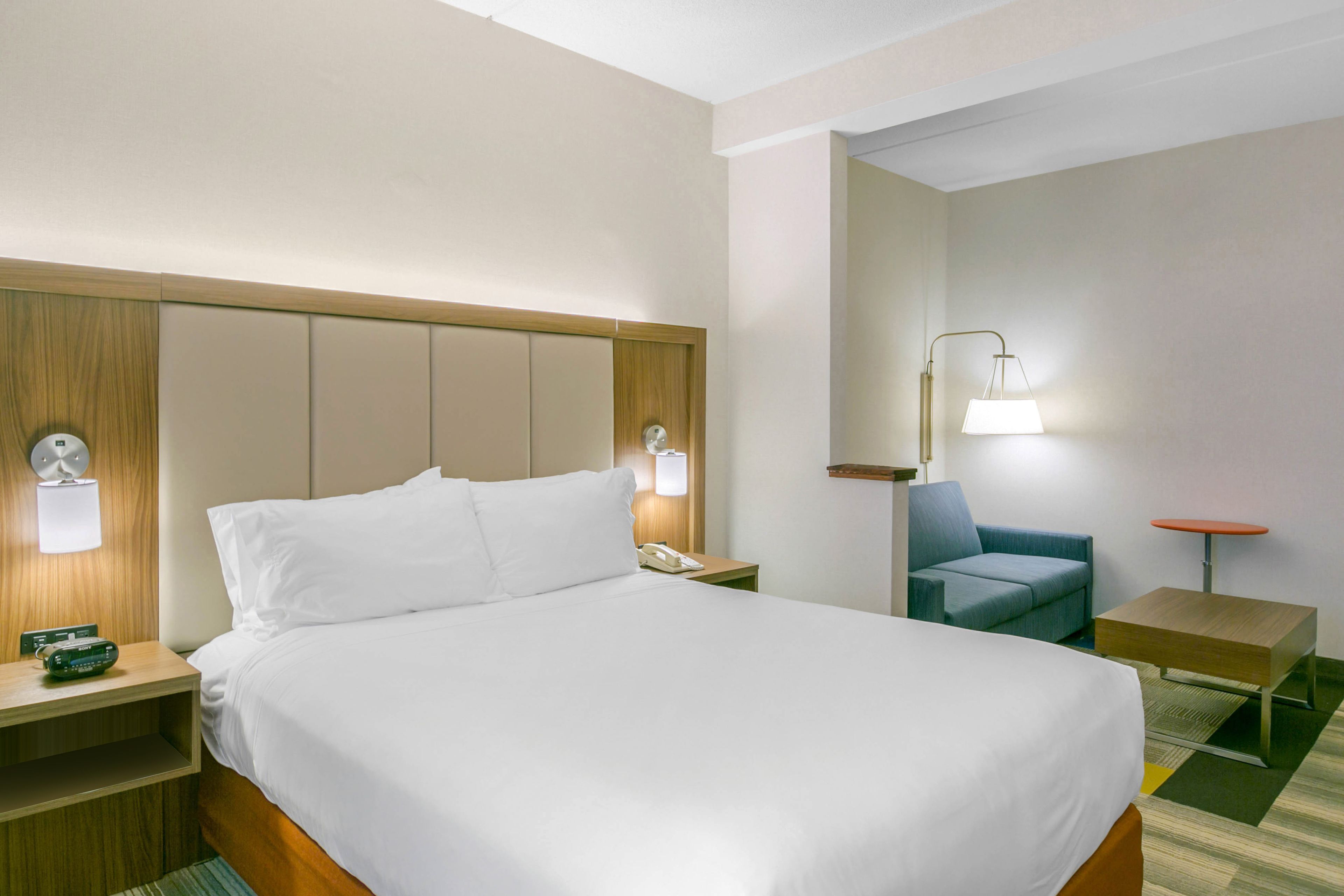 Una habitación de hotel con una cama grande, mesitas de noche, un escritorio, una silla y una lámpara.