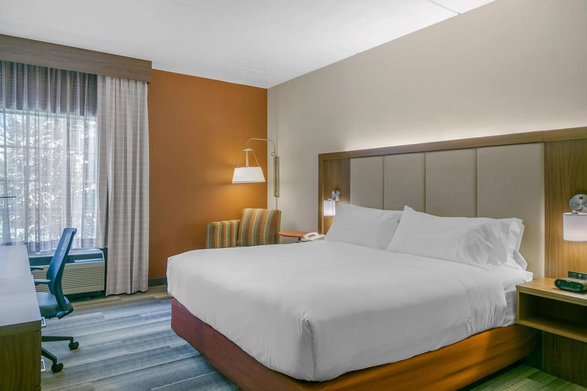 A hotel room with a large bed, a desk, a chair, a lamp, and a window with curtains.