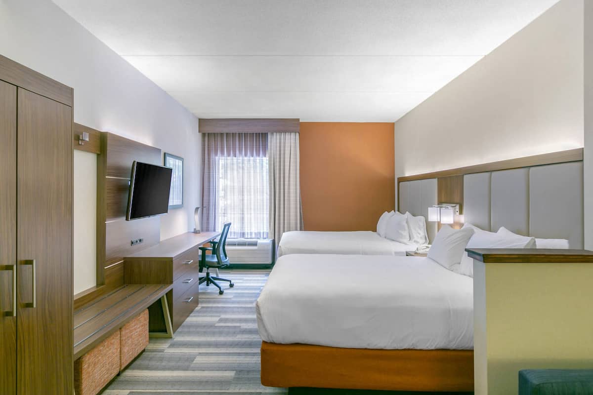A hotel room with two beds, a desk, a television, and a window with curtains.