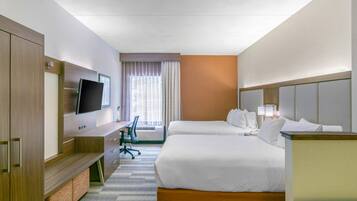 A hotel room with two beds, a desk, a television, and a window with curtains.