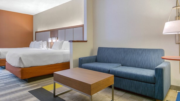 A hotel room with a bed, a sofa, a small table, and a lamp.