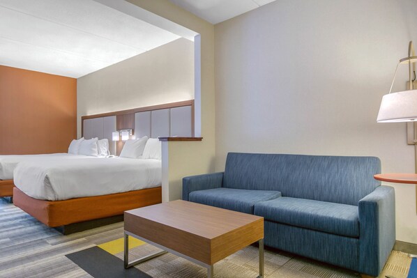 A hotel room with a bed, a sofa, a small table, and a lamp.
