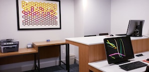 Een moderne kantoorruimte met een bureau, printer, computerscherm en een lijst met abstracte kunst aan de muur.