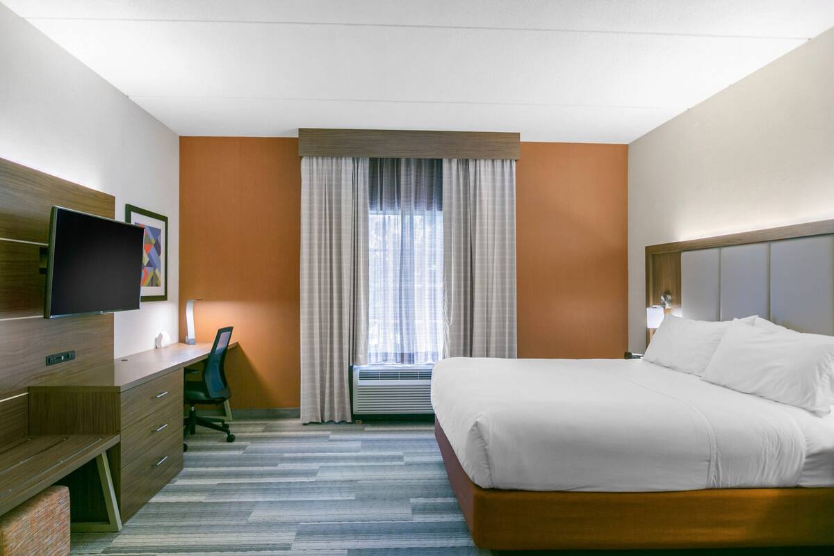 A hotel room with a bed, desk, chair, TV, and window with curtains.