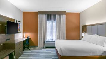 Habitación de hotel con cama, escritorio, silla, televisor y ventana con cortinas.