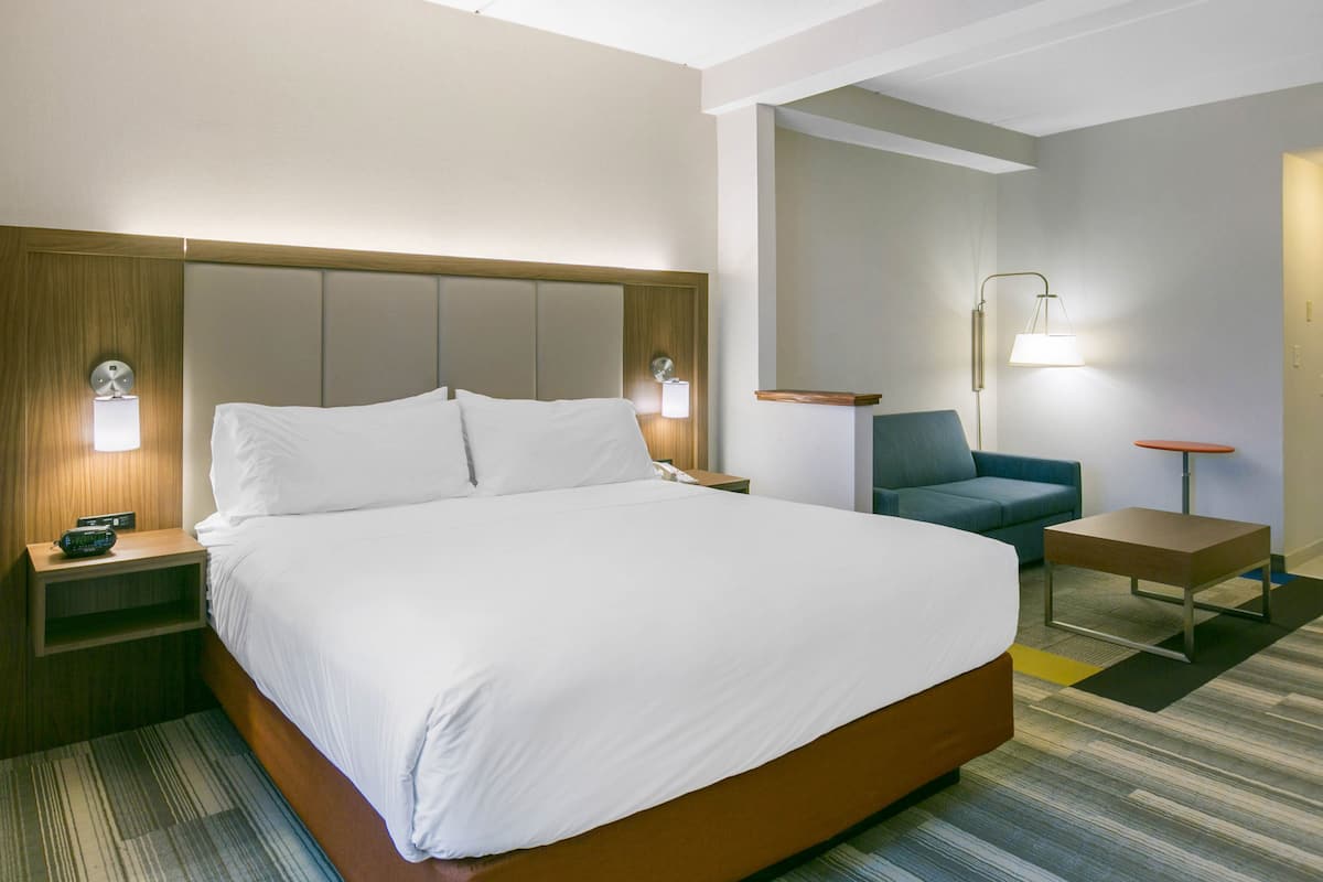 A hotel room with a large bed, bedside tables, a chair, a desk, and a lamp.