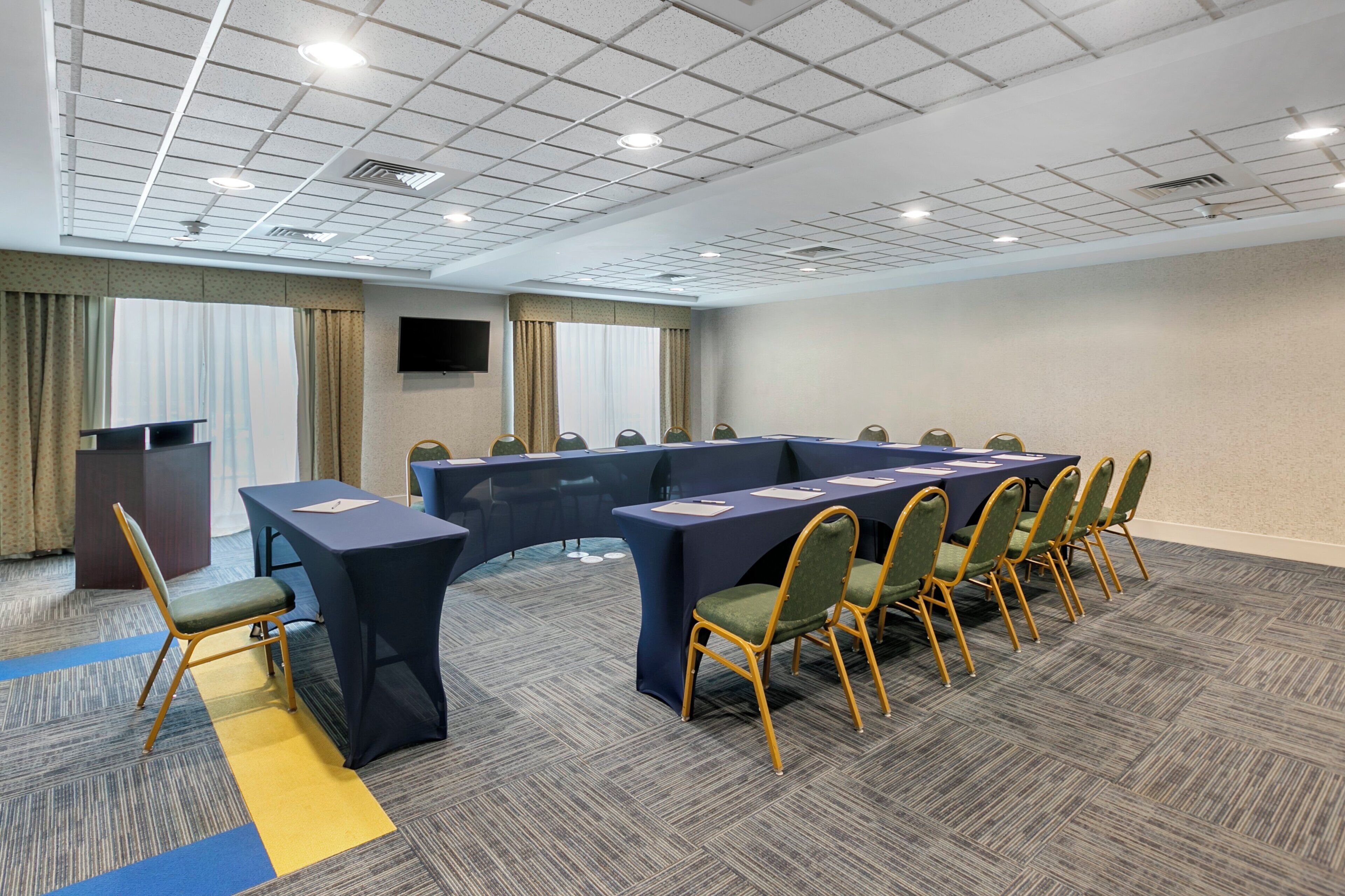 A conference room with a long table, chairs, a podium, and a television screen.