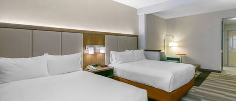 A hotel room with two beds, a nightstand with a lamp, and a door leading to another room.