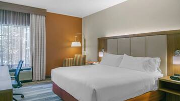 A hotel room with a large bed, a desk, a chair, a lamp, and a window with curtains.