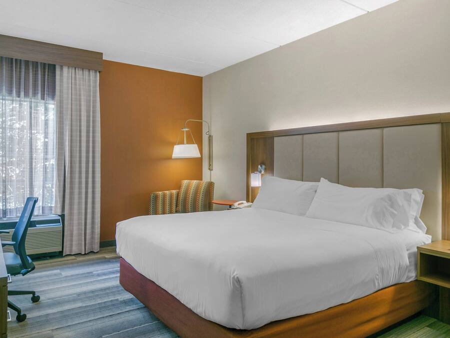 A hotel room with a large bed, a desk, a chair, a lamp, and a window with curtains.