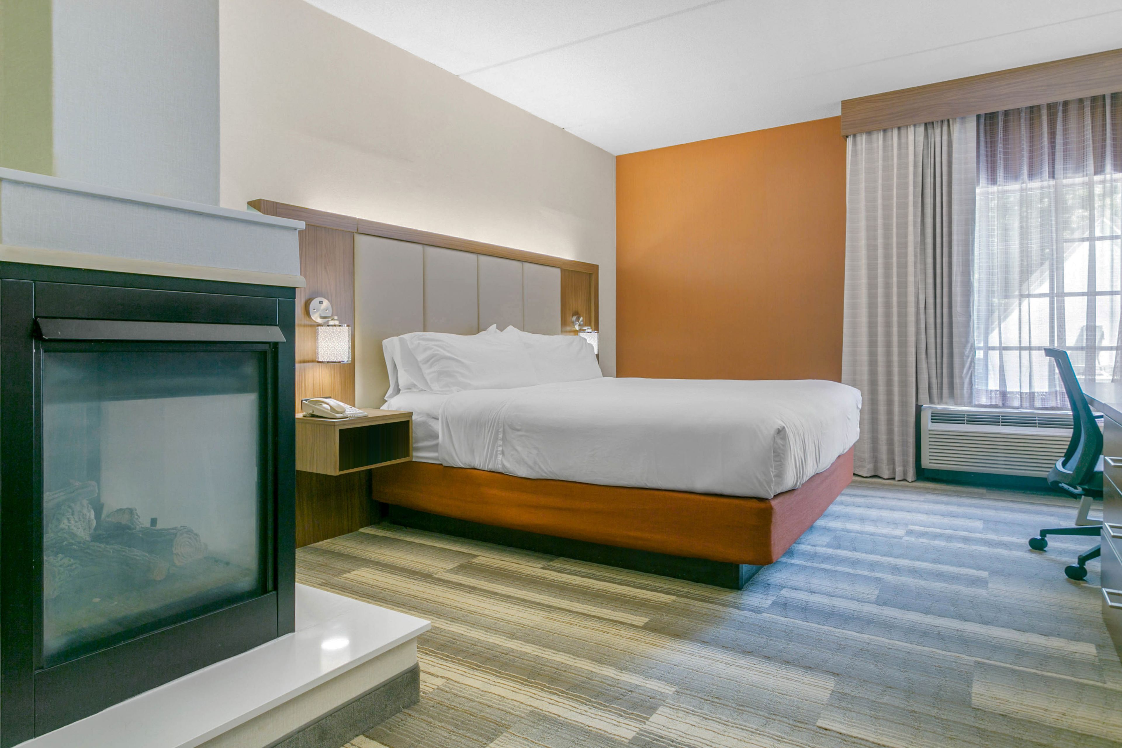 Habitación de hotel con cama, mesita de noche, lámpara, televisor y ventana con cortinas.
