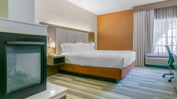Habitación de hotel con cama, mesita de noche, lámpara, televisor y ventana con cortinas.