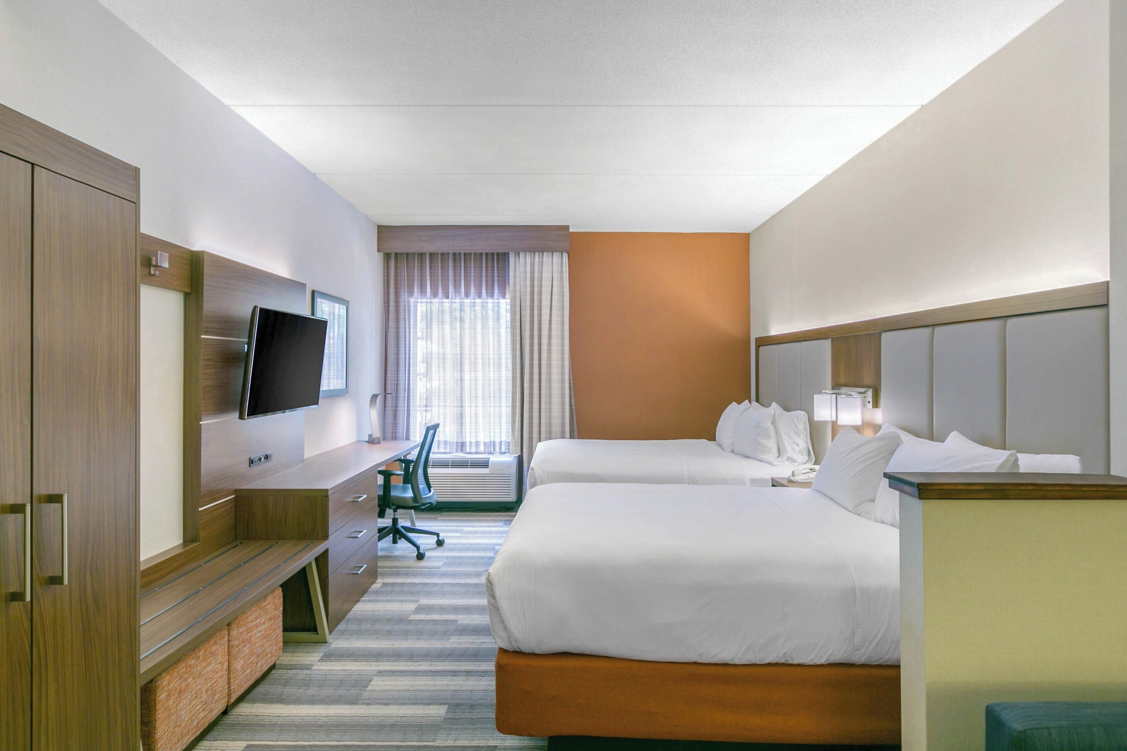 A hotel room with two beds, a desk, a chair, a TV, and a window with curtains.