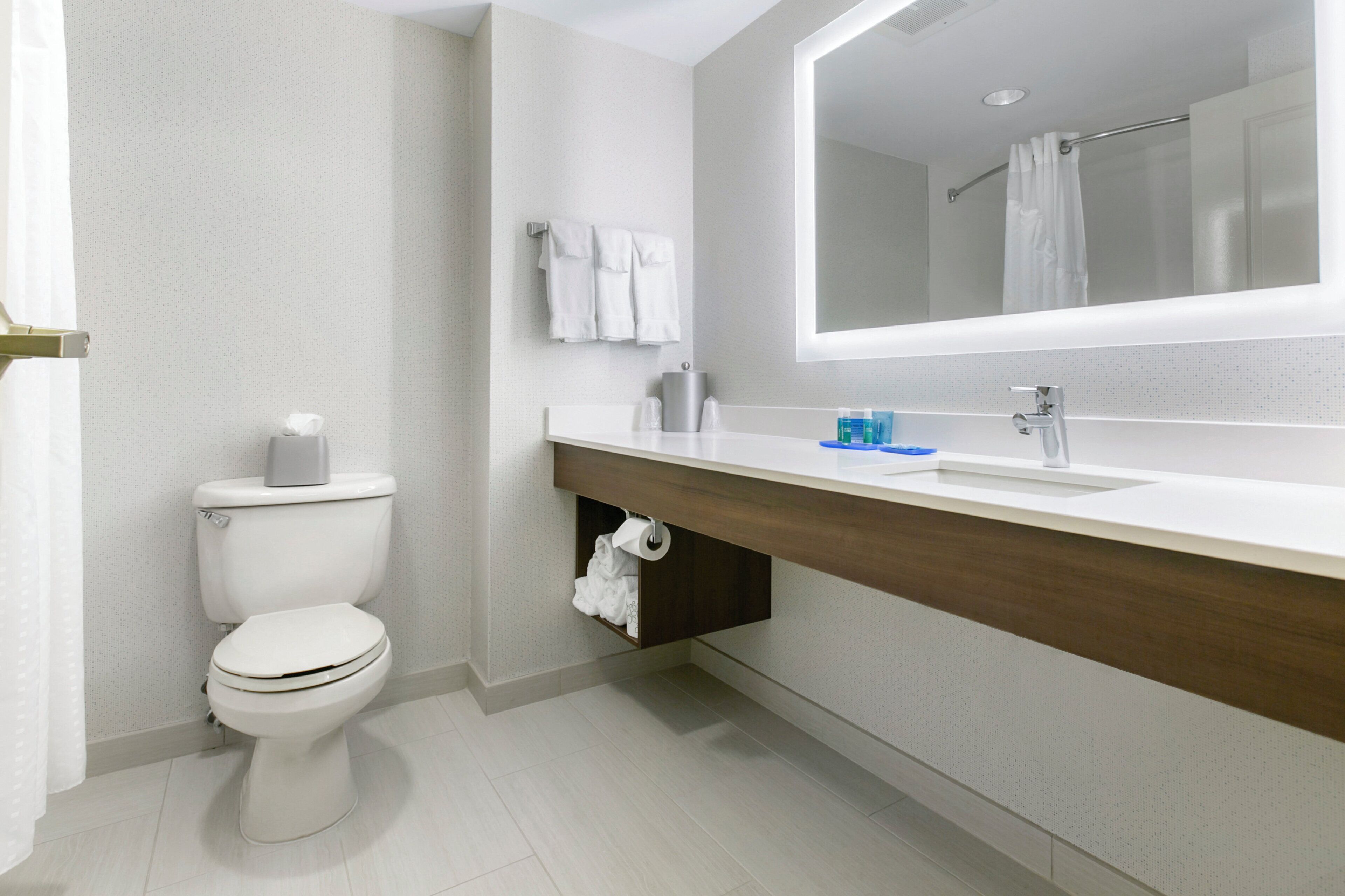 Un baño moderno con inodoro, lavamanos, espejo y toallero.