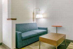 Een kamer met een blauwe bank, een houten tafel en een lamp aan de muur.