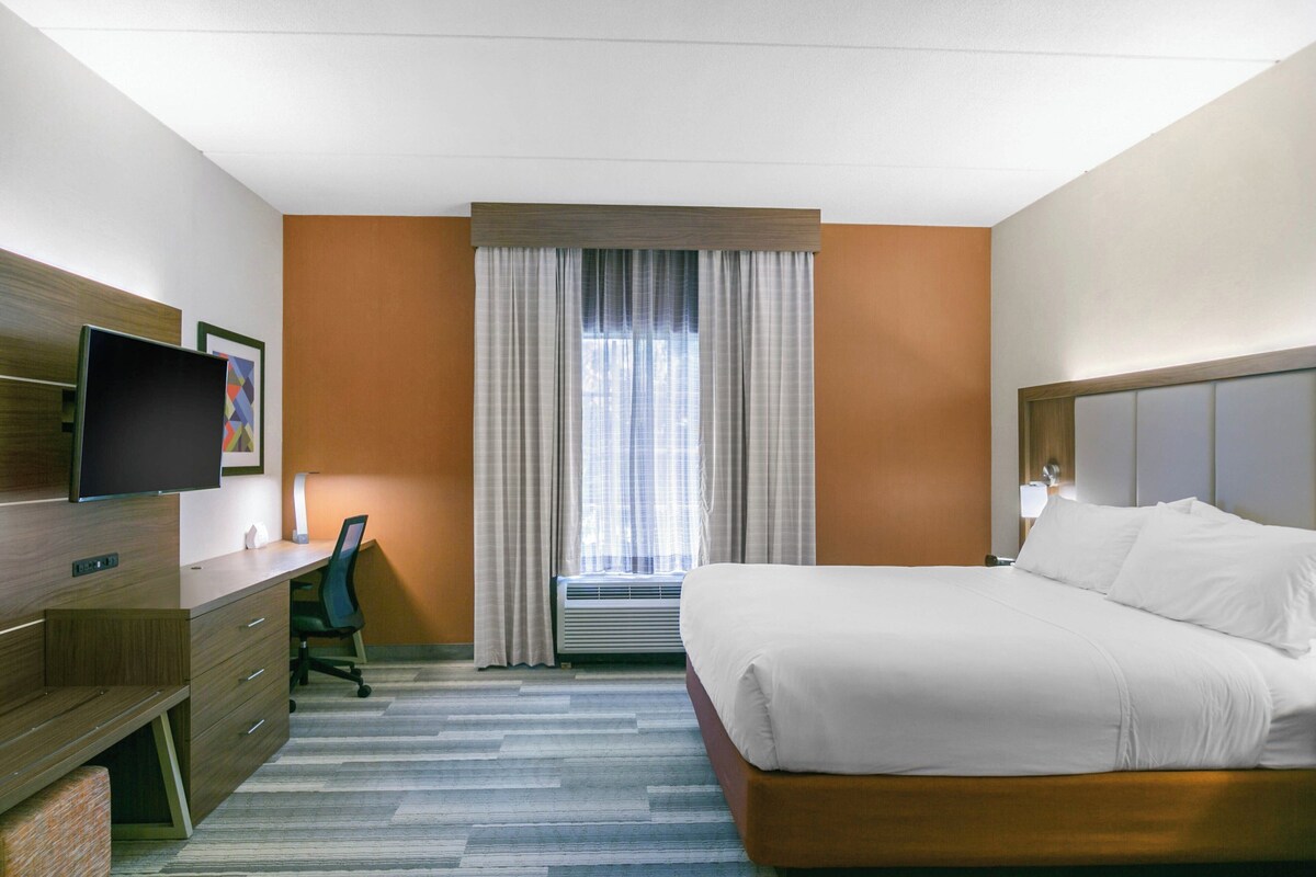 A hotel room with a bed, desk, chair, TV, and window with curtains.