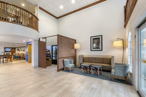 A hotel lobby with a wooden staircase, a seating area with a sofa and chairs, a television, and a vending machine. - Holiday Inn Express Hotel & Stes Mt. Arlington Rockaway Area by IHG (Mount Arlington)