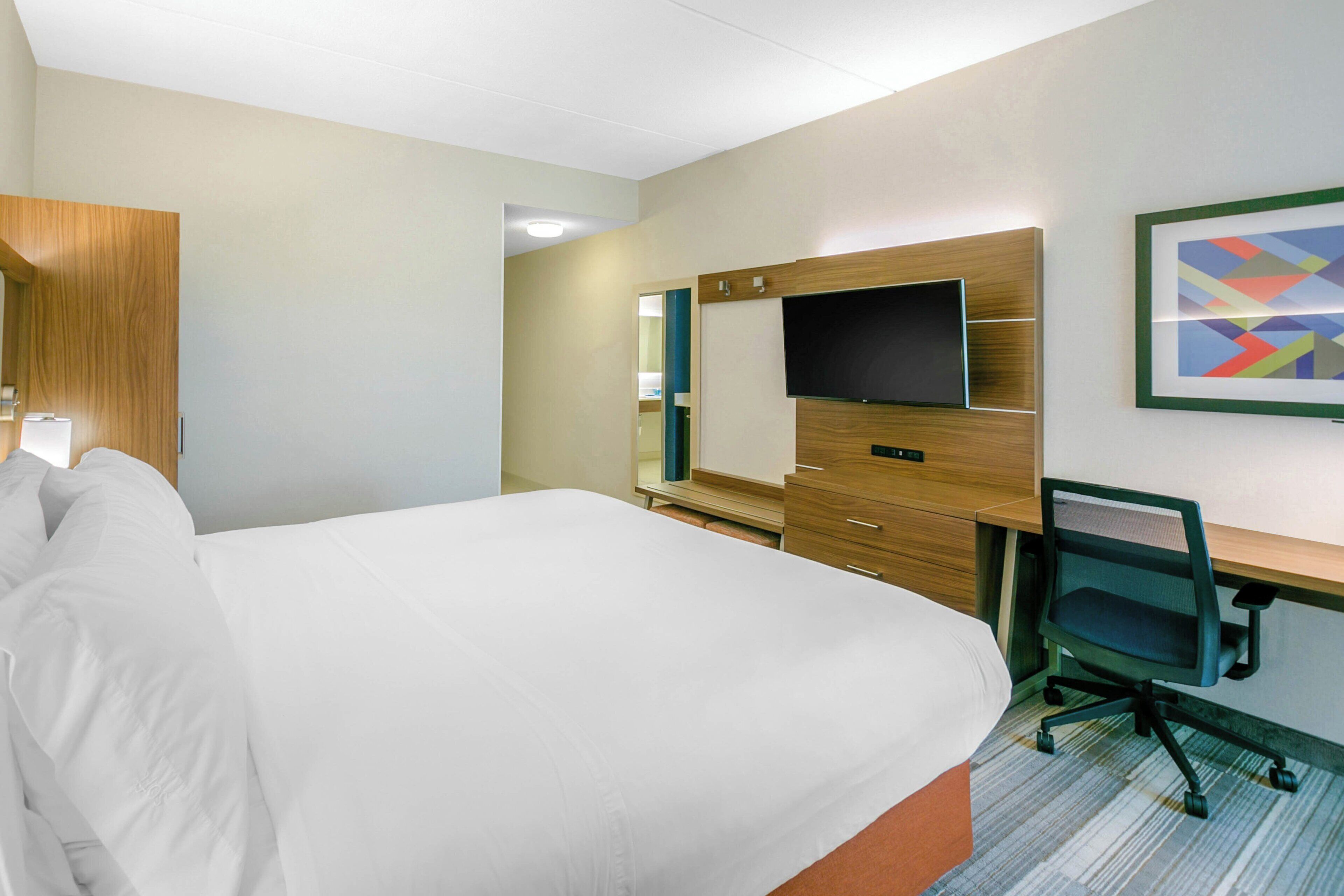 A hotel room with a bed, a desk, a chair, a television, and a mirror.