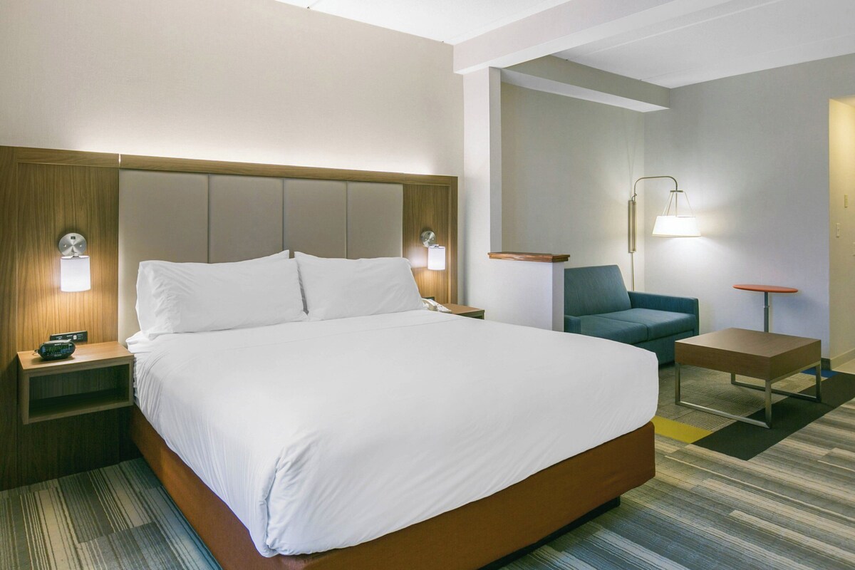 A hotel room with a large bed, bedside tables, a chair, and a desk.