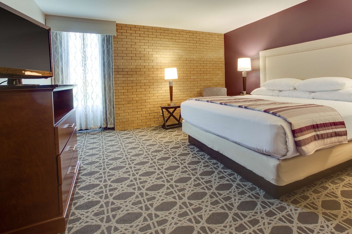 Una habitación de hotel con una pared de ladrillo, una cama con ropa blanca, un televisor sobre una cómoda de madera y una alfombra estampada.