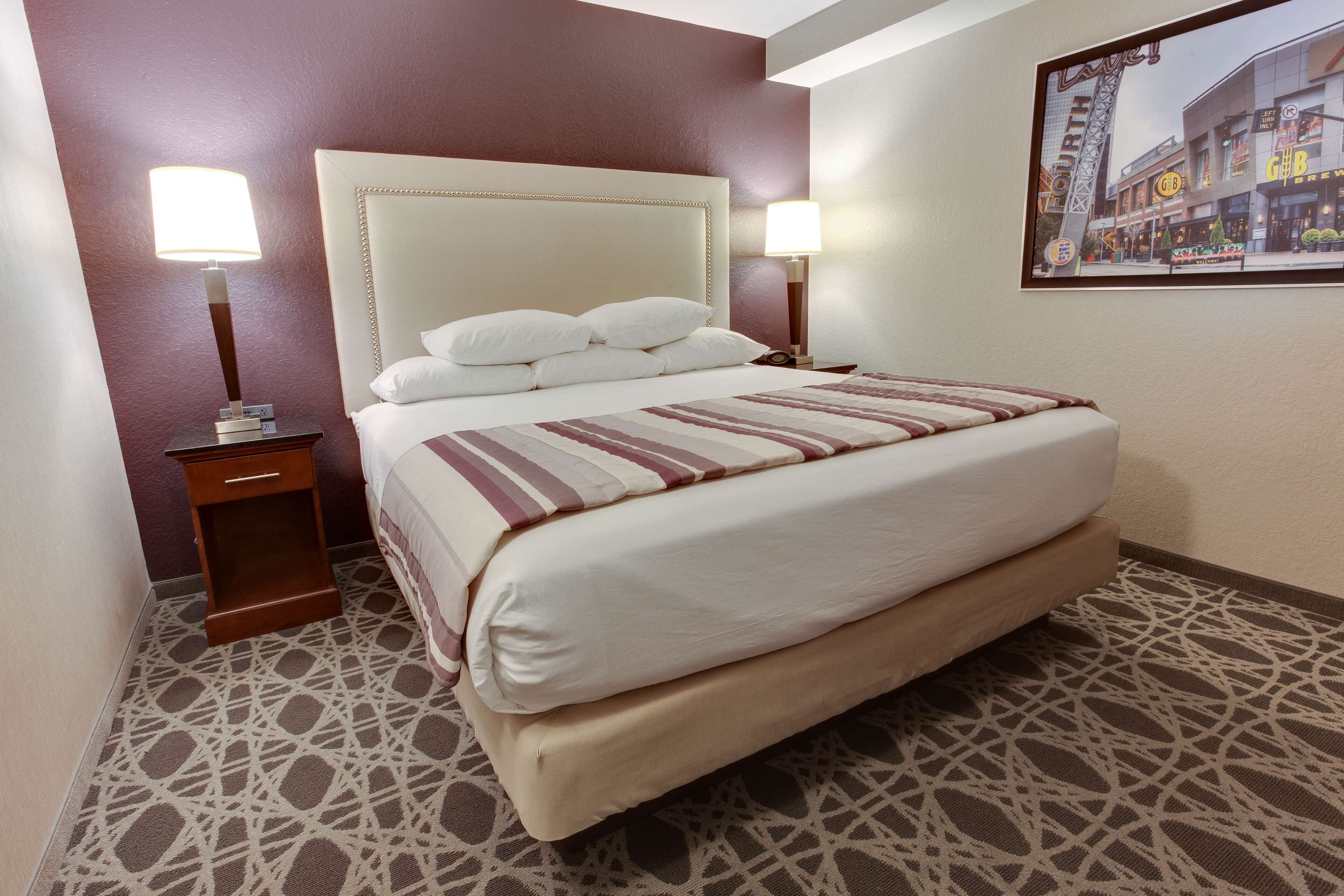 A hotel room with a large bed, two bedside tables, and a framed picture on the wall.