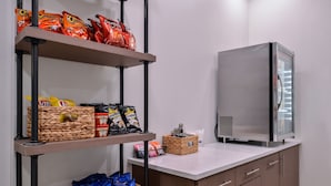 A kitchenette with a refrigerator, shelves with snack bags, and storage baskets. - Holiday Inn Express New Orleans - Arts District by IHG (New Orleans)