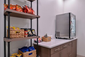 A kitchenette with a refrigerator, shelves with snack bags, and storage baskets. - Holiday Inn Express New Orleans - Arts District by IHG (New Orleans)