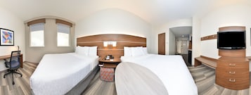 A hotel room with two beds, a desk with a chair, a television, and a bathroom visible through an archway.