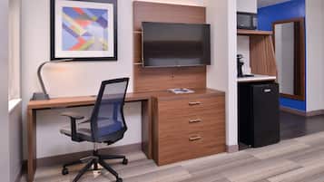 Um espaço de escritório moderno com uma mesa de madeira, uma cadeira de escritório preta, uma TV de tela plana fixada em um painel de madeira, uma máquina de café e uma geladeira.