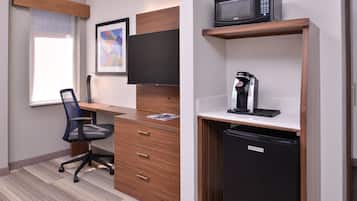 Un espacio de oficina moderno con un escritorio, una silla, televisor montado, cafetera y un refrigerador compacto.