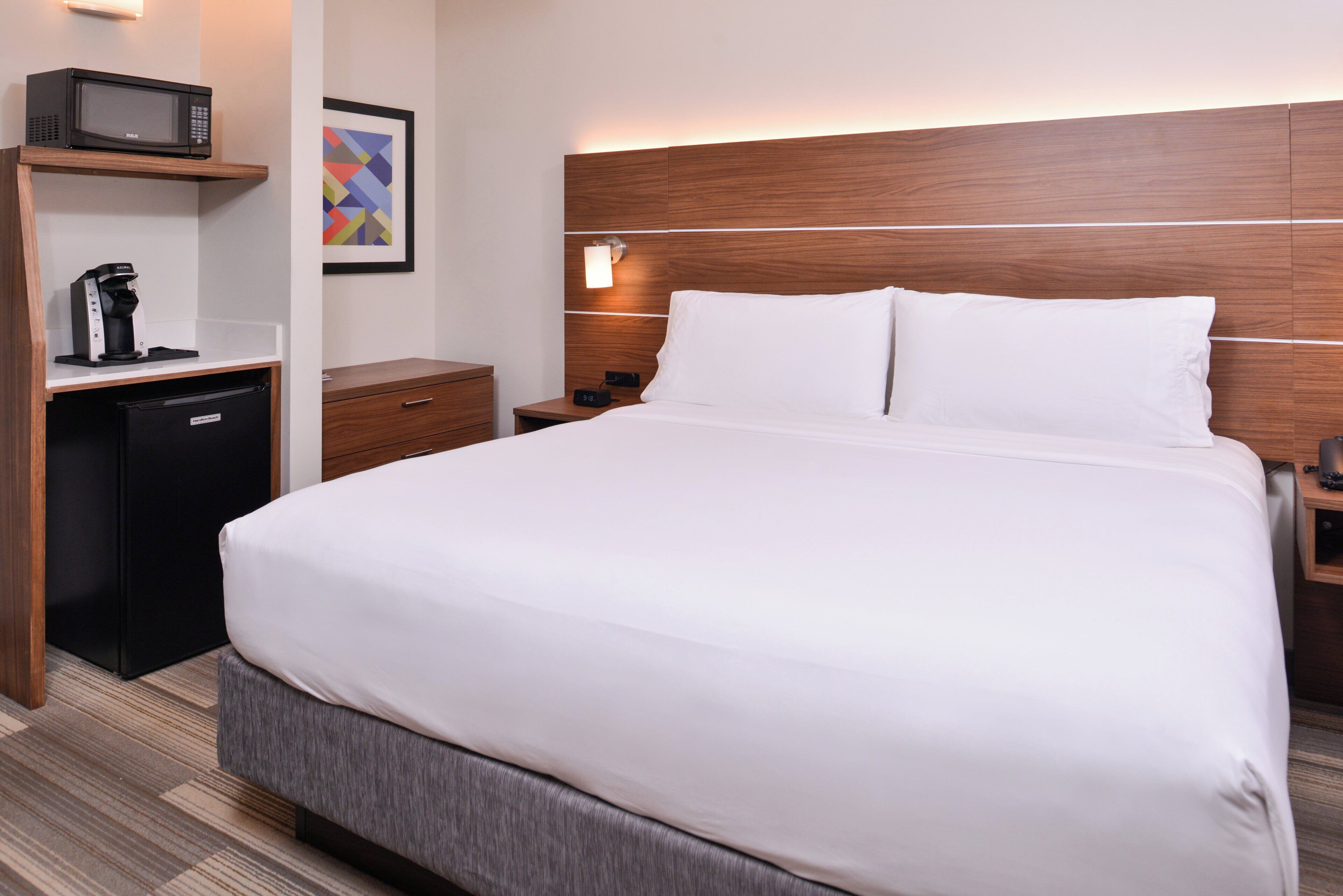 A hotel room with a bed, bedside tables, a microwave, a coffee maker, and a small cabinet.